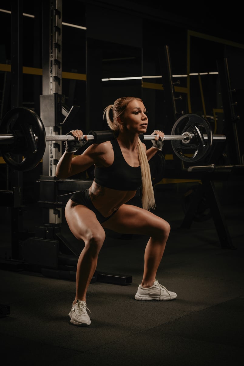 A fit woman is squatting with a barbell near the squat rack in a gym.